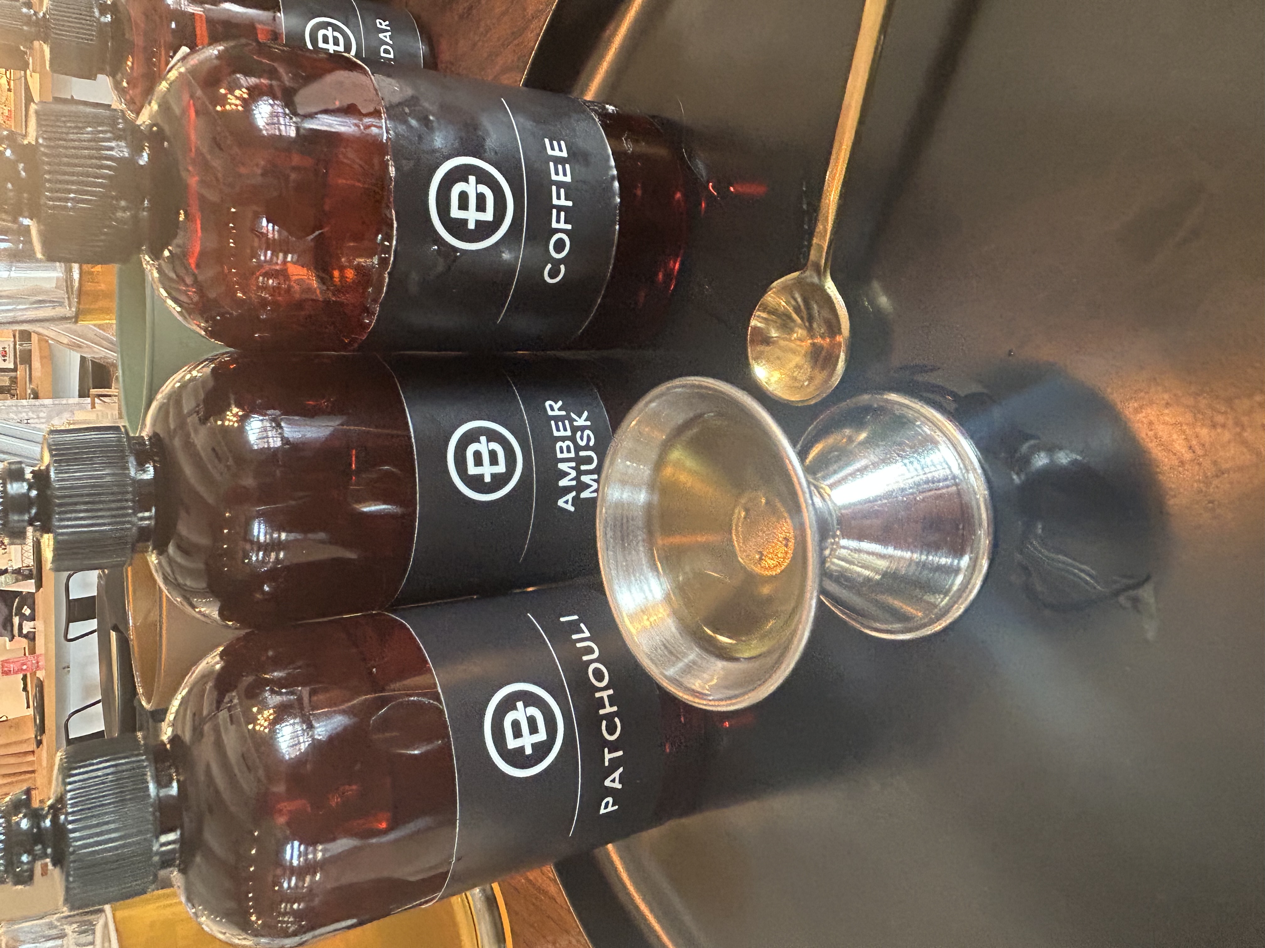 Patchouli, Amber Musk, and Coffee fragrance oils on a tray with a jigger and gold spoon