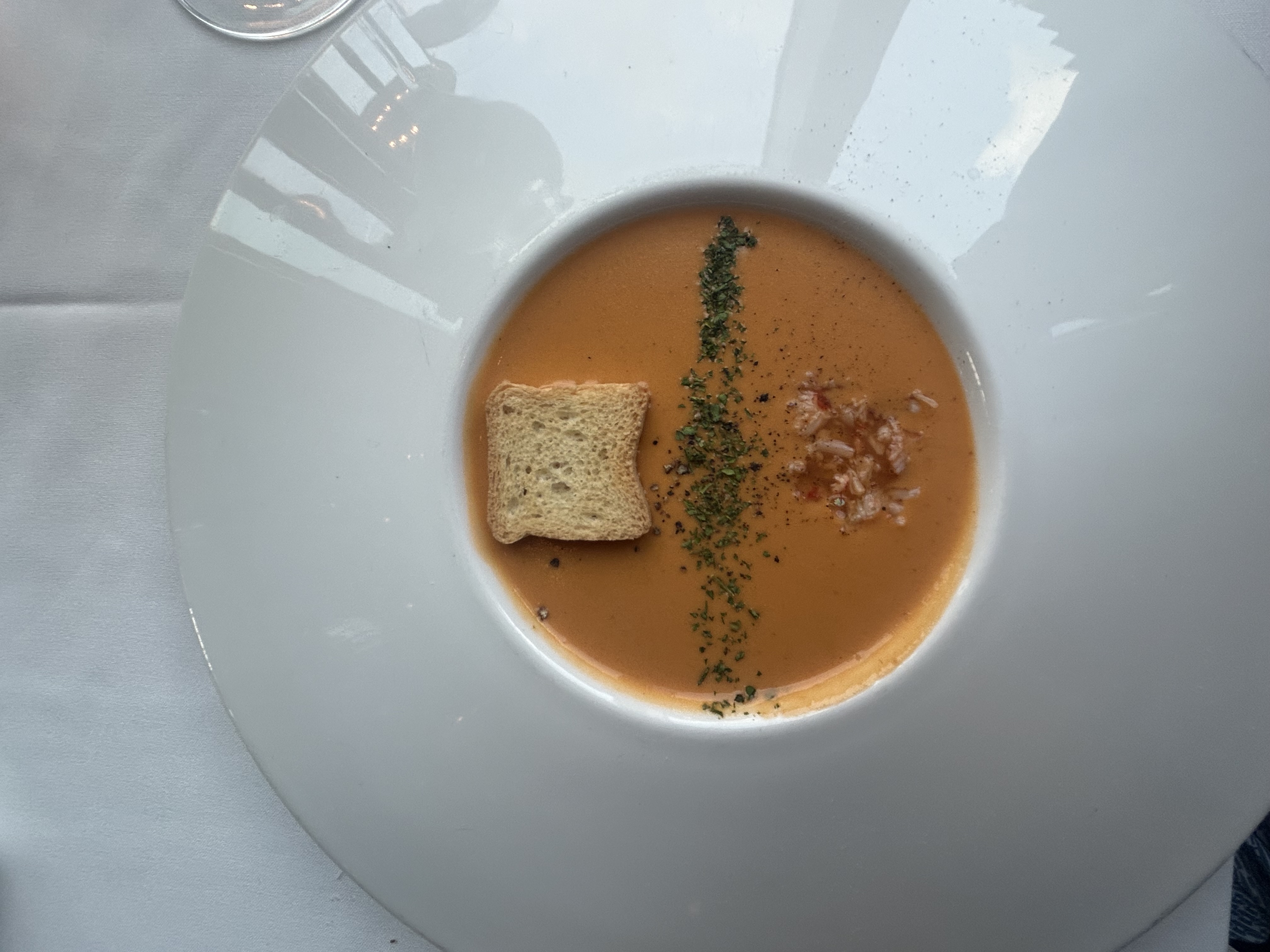 Lobster bisque with crab, herbs, and a crouton in a wide white bowl