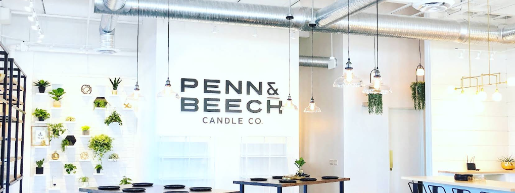 The bright white interior of Penn & Beech Candle Co. in Midtown Carmel, with hanging plants and pouring tables