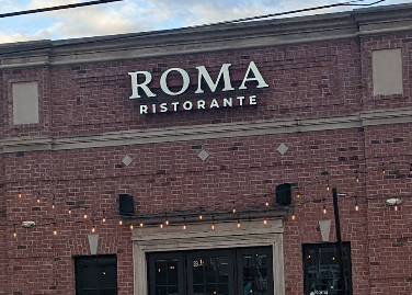The Roma Ristorante sign on the brick exterior at 89 Veterans Way in Midtown Carmel, with string lights over the patio