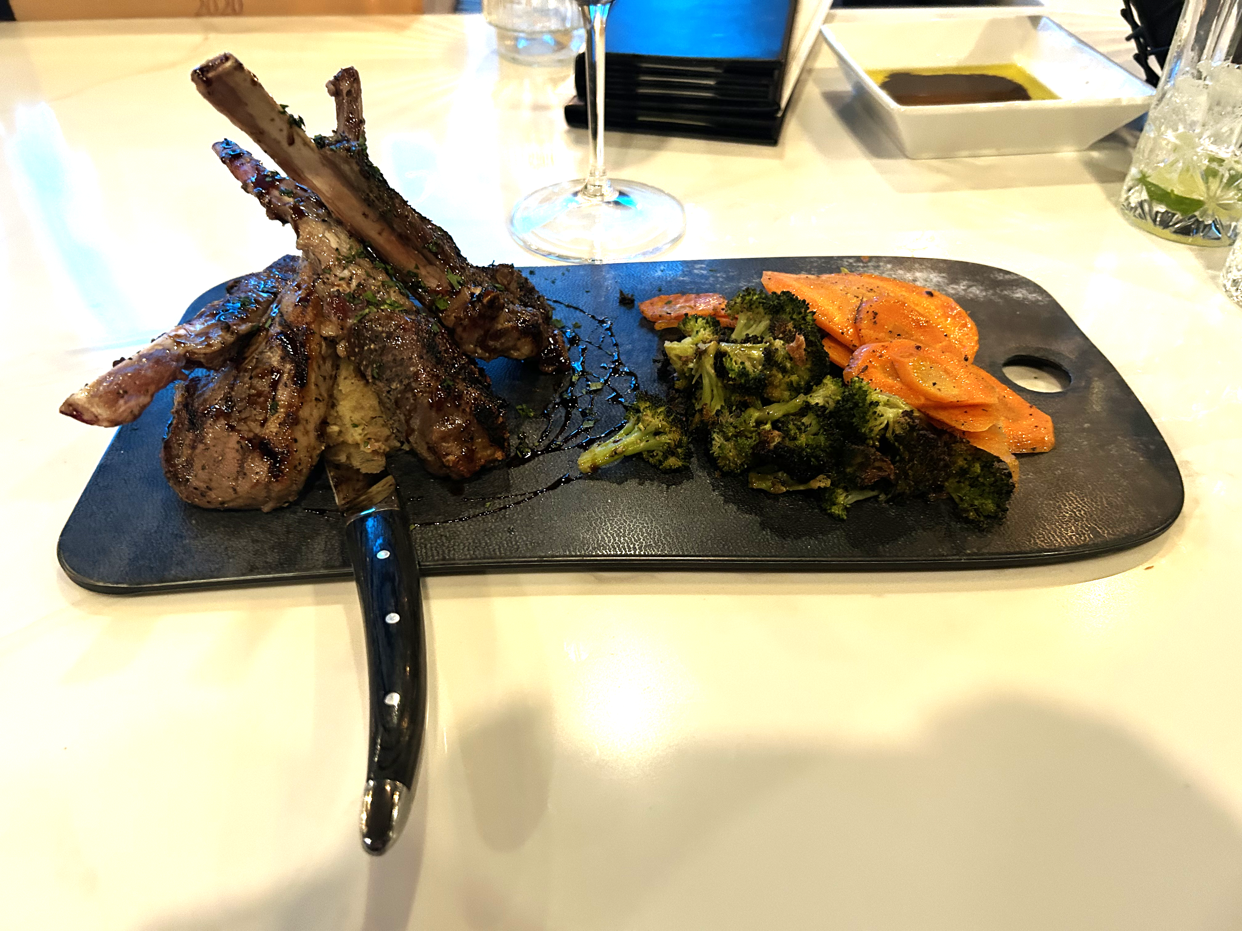 Grilled lamb lollipops with balsamic reduction, broccoli, and carrots on a slate board at Ristorante Roma
